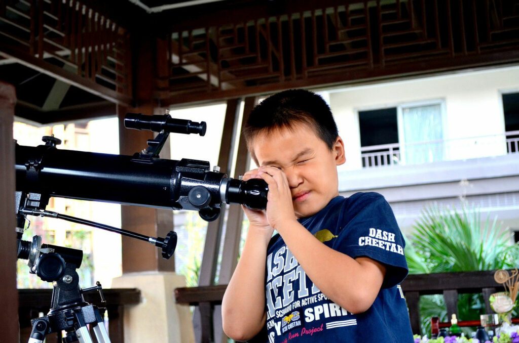 Little boy looking through a professional telescope outside, daytime, getting excited about astronomy